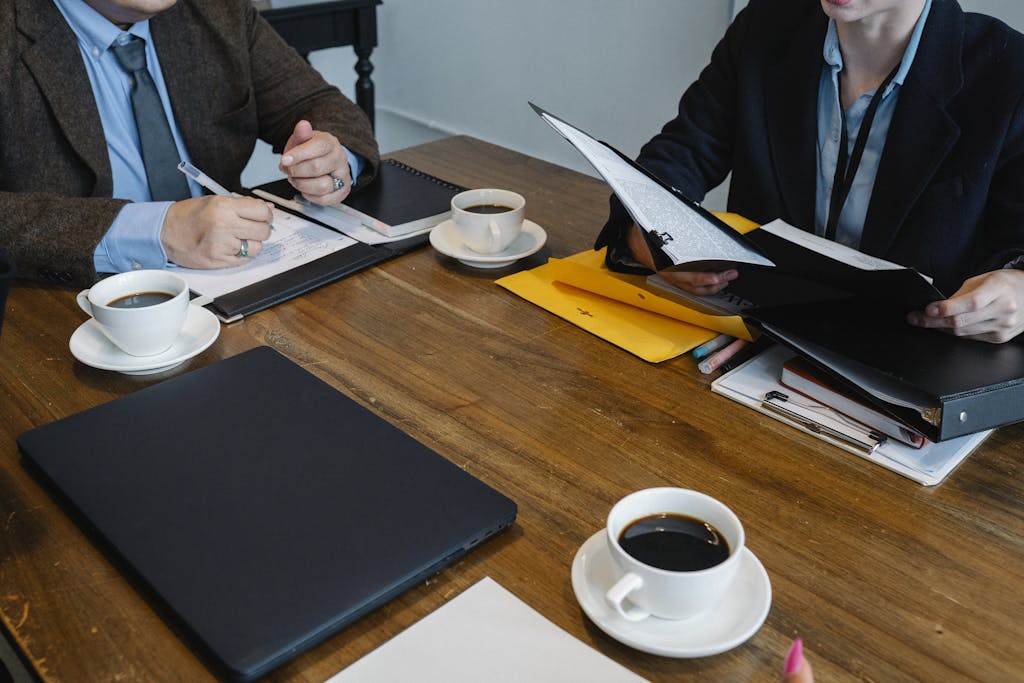 Crop unrecognizable coworkers in formal clothes sitting at table with documents and cups of coffee while working together
